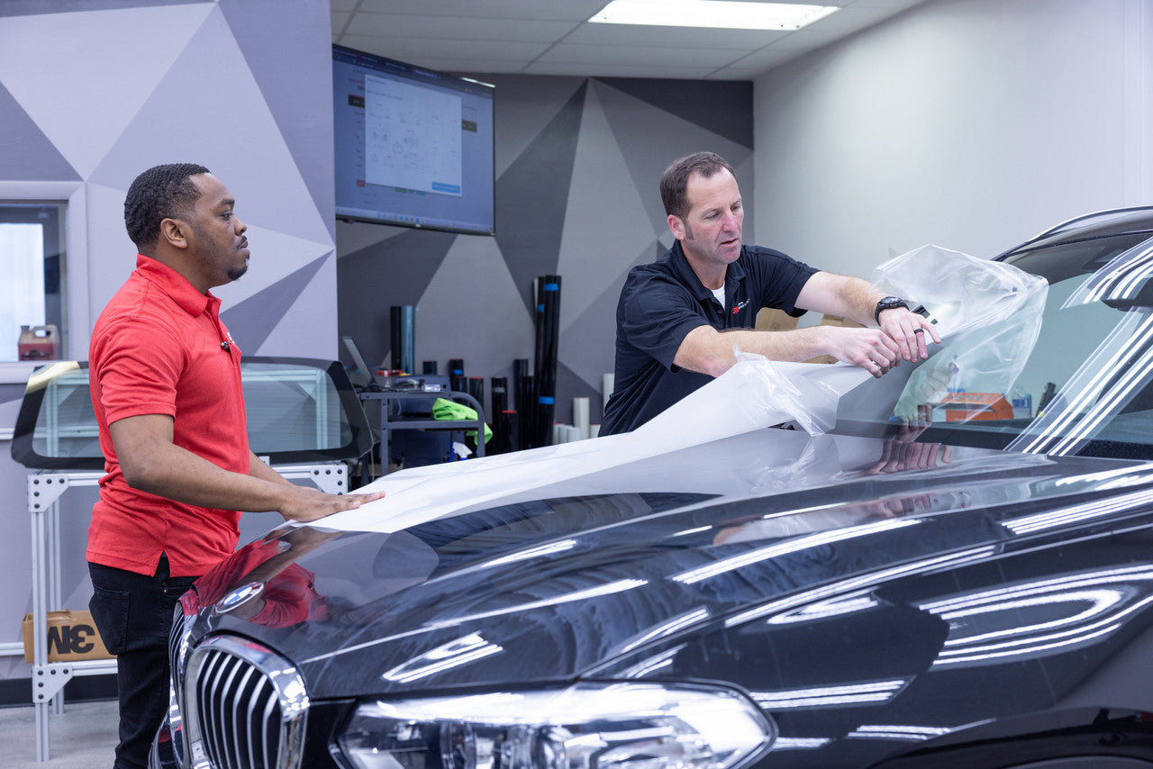 installation instructor placing wrap film on a car's window shield
