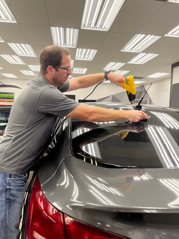 man using a heat gun to apply tint on back of car window