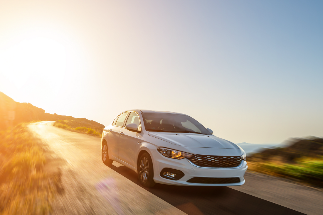 white car driving down a hill at sunset