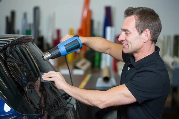 installer using a squeegee and heat gun to install window tint on car